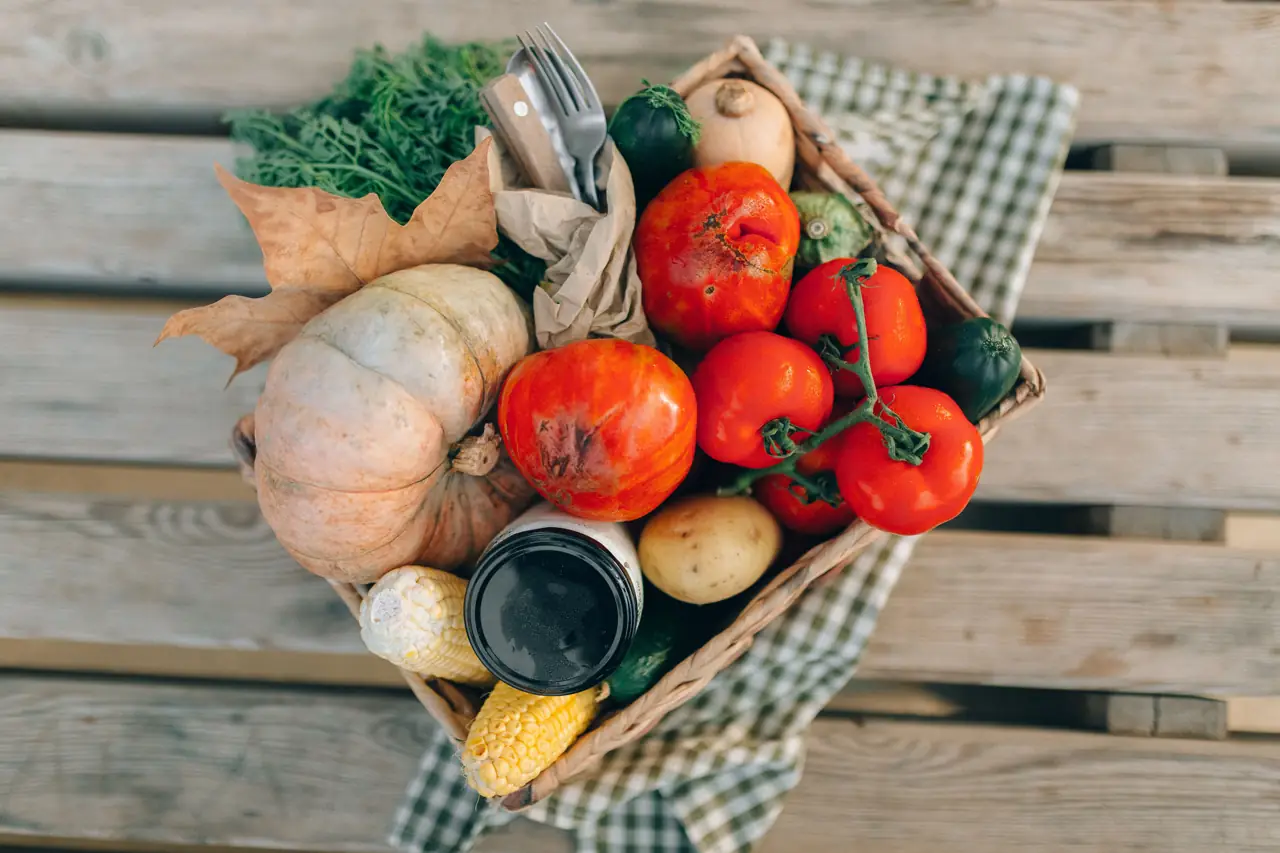 A basket of organic pumpkin, tomatoes, corn and vegetables on a wooden table
